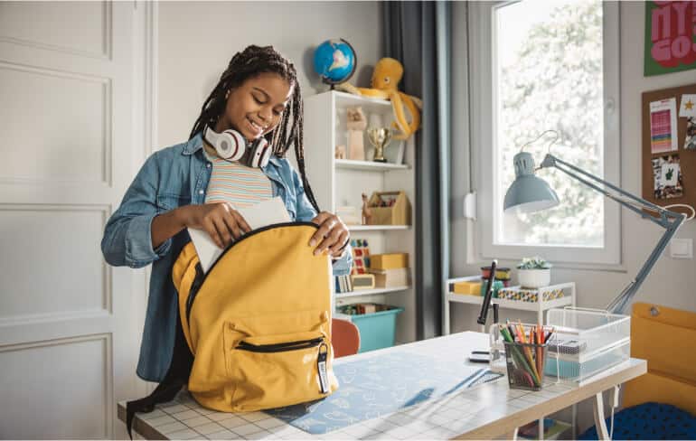 Student packing supplies in a backpack